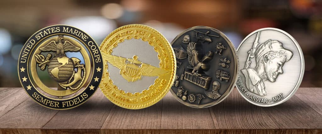 Collection of custom promotional coins and medals including military, sports, and commemorative designs displayed on a wooden surface.